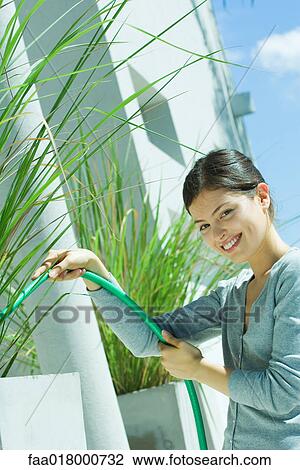 Stock Image - Young woman watering plants with garden hose. Fotosearch