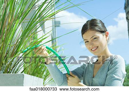 Stock Image - Young woman watering plants with garden hose. Fotosearch