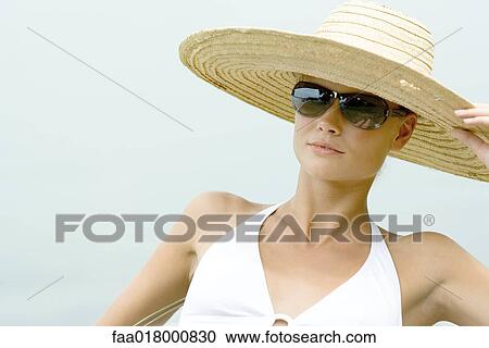 Stock Image - Young woman wearing sunhat and sunglasses. Fotosearch