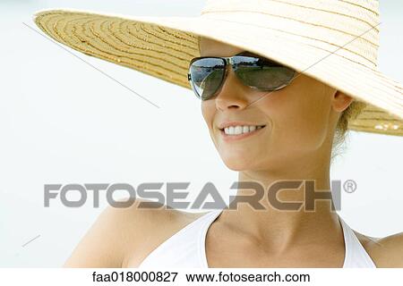 Stock Photo - Young woman wearing sunhat and sunglasses, smiling. Fotosearch