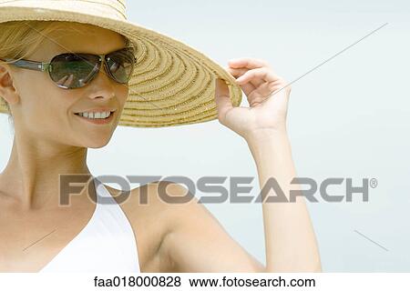 Stock Photo - Young woman wearing sunhat and sunglasses, smiling. Fotosearch