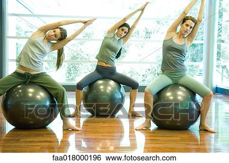 Stock Photograph - Young women sitting on fitness balls, doing side stretch. Fotosearch
