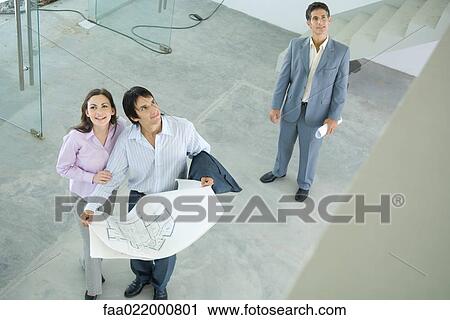 Stock Image - Architect showing unfinished house to enthusiastic young couple, high angle view. Fotosearch
