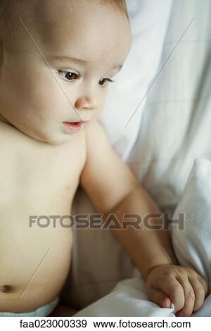 Baby in bed with hand on blanket, looking down, close-up View Large Photo Image Stock Photo - Baby in bed with hand on blanket, looking down, close-up. Fotosearch