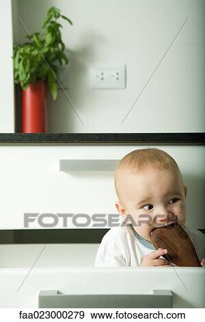 Baby in drawer, biting on wooden spoon, making funny face View Large Photo Image Stock Photo - Baby in drawer, biting on wooden spoon, making funny face. Fotosearch