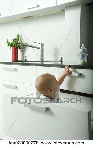 Baby in drawer reaching for bottle on kitchen counter View Large Photo Image Stock Photo - Baby in drawer reaching for bottle on kitchen counter. Fotosearch