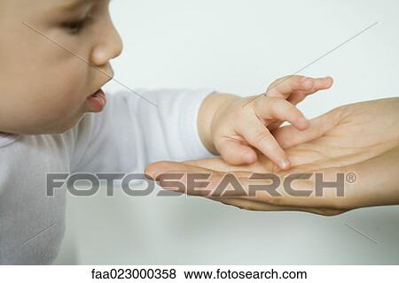 Stock Photo - Baby inspecting mother's palm, close-up, cropped view. Fotosearch