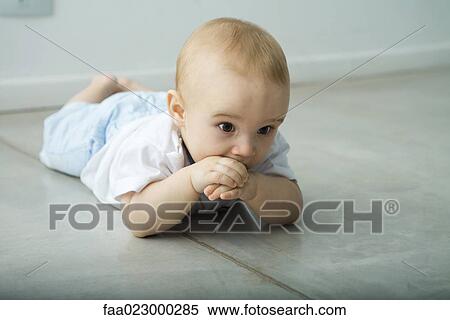 Baby lying on floor, hand in mouth View Large Photo Image Stock Photography - Baby lying on floor, hand in mouth. Fotosearch