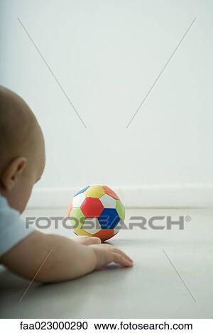 Stock Image - Baby lying on floor, looking at ball. Fotosearch