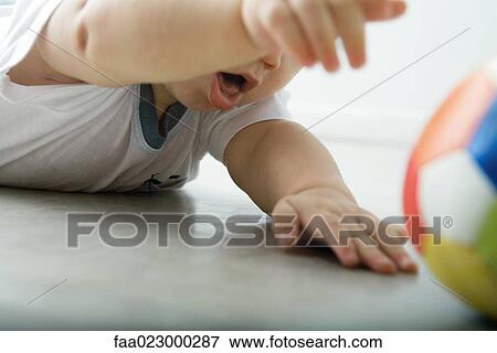 Baby lying on floor, reaching for ball, cropped view View Large Photo Image Stock Photo - Baby lying on floor, reaching for ball, cropped view. Fotosearch