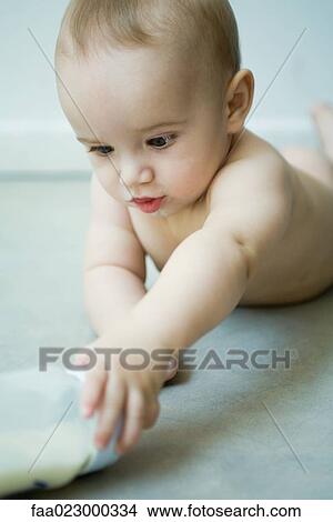 Picture - Baby lying on floor, reaching for bottle. Fotosearch
