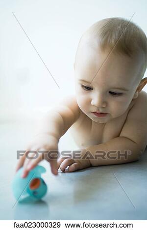 Stock Photo - Baby lying on floor, reaching for rubber duck. Fotosearch