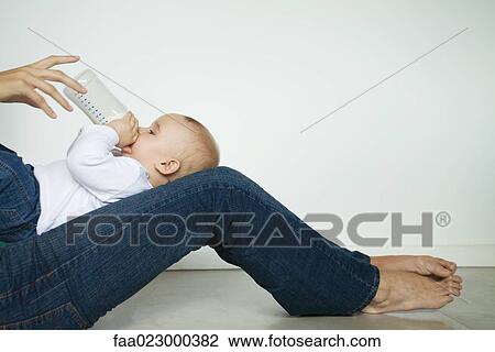 Baby lying on mother's legs, drinking from bottle, side view View Large Photo Image Stock Image - Baby lying on mother's legs, drinking from bottle, side view. Fotosearch