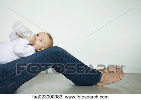 Baby lying on mother's legs, drinking from bottle, side view View Large Photo Image Stock Image - Baby lying on mother's legs, drinking from bottle, side view. Fotosearch