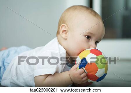 Stock Image - Baby on floor, holding ball up to mouth. Fotosearch