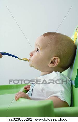 Baby sitting in high chair, being fed, looking up View Large Photo Image Stock Image - Baby sitting in high chair, being fed, looking up. Fotosearch