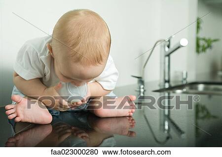 Baby sitting on kitchen counter, holding bottle, looking down at reflection View Large Photo Image Stock Image - Baby sitting on kitchen counter, holding bottle, looking down at reflection. Fotosearch