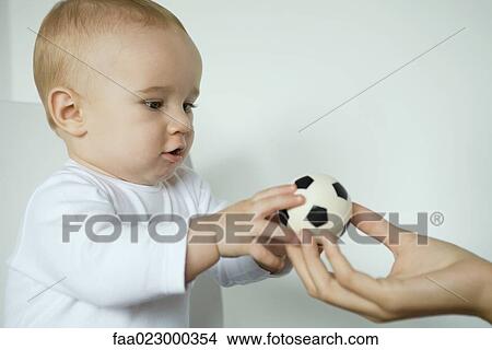 Picture - Baby taking ball from mother's hand, close-up. Fotosearch