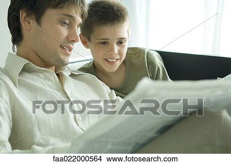 Boy and father reading newspaper together on sofa View Large Photo Image Picture - Boy and father reading newspaper together on sofa. Fotosearch