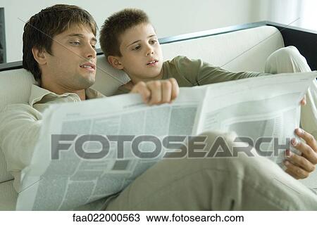 Boy and father reading newspaper together on sofa View Large Photo Image Stock Image - Boy and father reading newspaper together on sofa. Fotosearch
