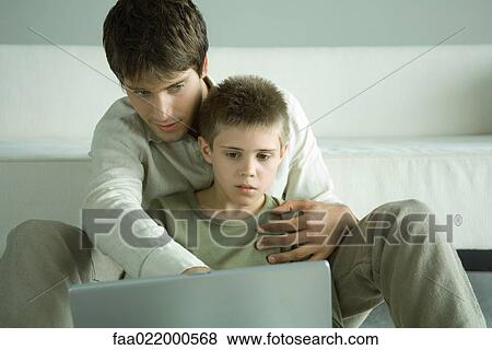 Stock Photo - Boy and father using laptop together. Fotosearch