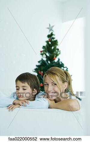 Stock Image - Boy and mother on sofa, Christmas tree in background, woman smiling at camera, boy frowning. Fotosearch