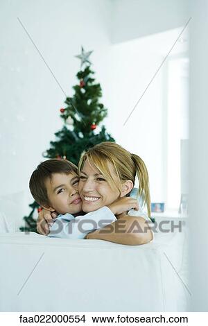 Boy and mother on sofa hugging each other, Christmas tree in background View Large Photo Image Picture - Boy and mother on sofa hugging each other, Christmas tree in background. Fotosearch
