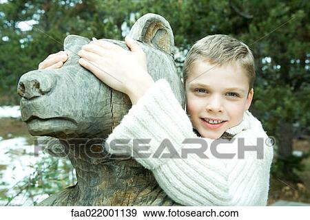 Stock Photo - Boy embracing bear statue, covering its eyes with his hands, smiling at camera. Fotosearch