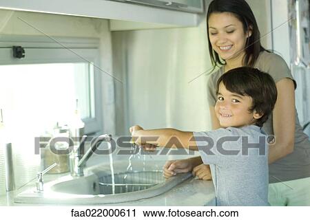Boy helping mother wash dishes, looking over shoulder at camera View Large Photo Image Stock Image - Boy helping mother wash dishes, looking over shoulder at camera. Fotosearch