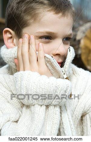 Stock Photography - Boy holding collar of wool sweater over face, close-up, portrait. Fotosearch