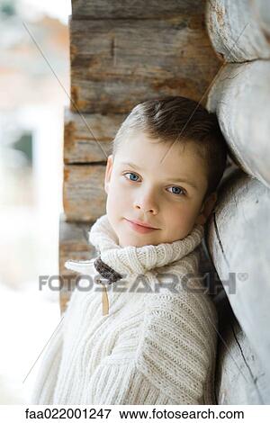 Stock Photo - Boy leaning against wood cabin, smiling at camera. Fotosearch