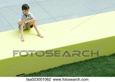 Boy sitting on low wall, looking at cell phone, squinting View Large Photo Image Stock Image - Boy sitting on low wall, looking at cell phone, squinting. Fotosearch