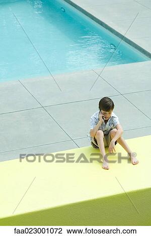 Boy sitting on the ground in front of swimming pool, using cell phone, looking down View Large Photo Image Stock Image - Boy sitting on the ground in front of swimming pool, using cell phone, looking down. Fotosearch
