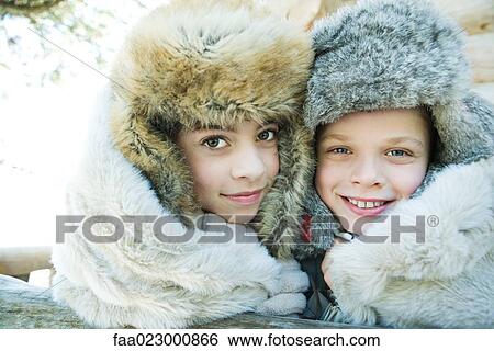 Stock Photograph - Brother and sister smiling at camera, cheek to cheek, both wearing fur caps, portrait. Fotosearch
