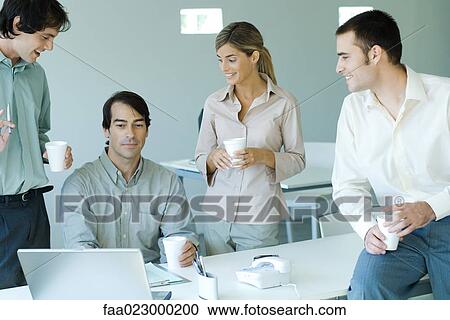 Business associates gathered around male colleague seated at laptop, all holding disposable cups View Large Photo Image Stock Image - Business associates gathered around male colleague seated at laptop, all holding disposable cups. Fotosearch