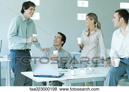 Stock Photo - Business associates gathered around table, holding disposable cups, laughing. Fotosearch