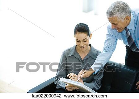 Stock Image - Business associates looking at file together, man pointing, looking over woman's shoulder. Fotosearch