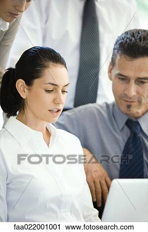 Stock Image - Business associates looking at laptop computer together, cropped view. Fotosearch