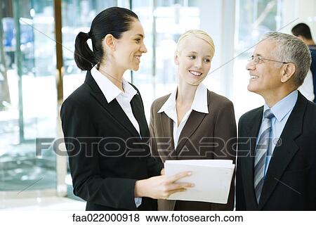 Business associates standing, smiling at each other, one holding binder View Large Photo Image Stock Photo - Business associates standing, smiling at each other, one holding binder. Fotosearch