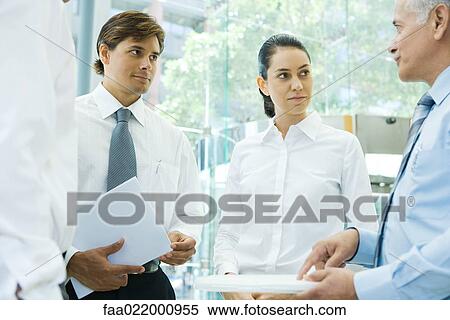 Stock Photography - Business associates standing together, discussing, one pointing at file. Fotosearch