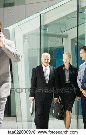 Stock Photo - Business associates walking together, smiling, building in background. Fotosearch