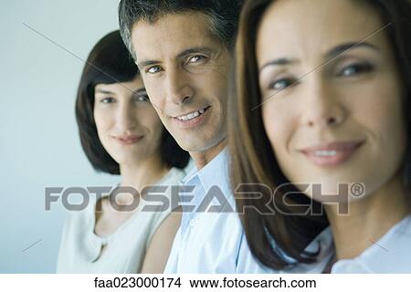 Picture - Business team in a row smiling at camera, head and shoulders, focus on man in middle, portrait. Fotosearch