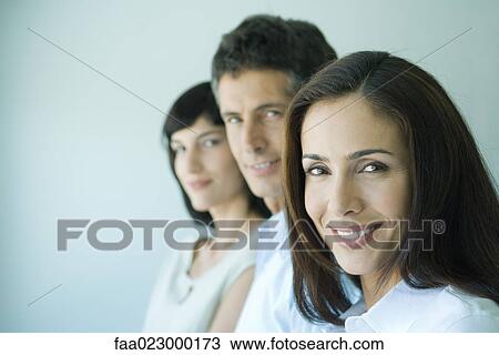 Stock Image - Business team in a row smiling at camera, head and shoulders, focus on woman in foreground, portrait. Fotosearch