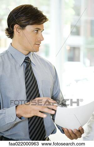 Stock Image - Businessman holding document, looking away, waist up. Fotosearch