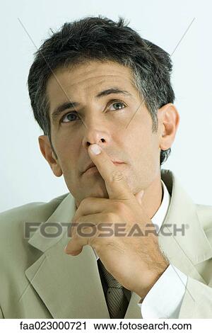 Stock Image - Businessman holding finger over lips, looking up. Fotosearch