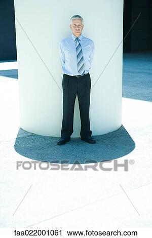 Businessman leaning against column outdoors, hands behind back, eyes closed View Large Photo Image Stock Image - Businessman leaning against column outdoors, hands behind back, eyes closed. Fotosearch