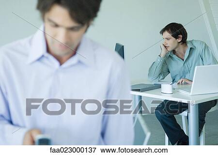 Businessman looking at computer, hand under chin, associate in foreground View Large Photo Image Stock Photo - Businessman looking at computer, hand under chin, associate in foreground. Fotosearch