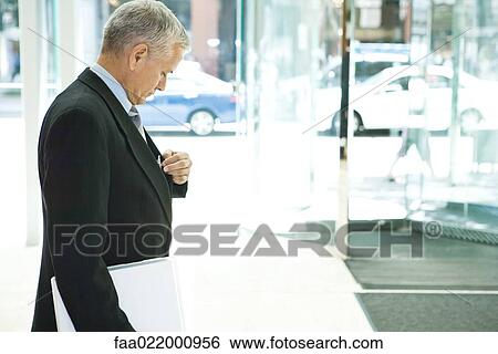 Businessman looking down, reaching for pen in pocket, side view View Large Photo Image Stock Photograph - Businessman looking down, reaching for pen in pocket, side view. Fotosearch