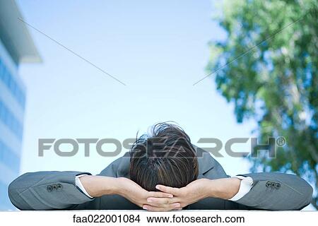 Picture - Businessman lying on back outdoors, hands behind head, rear view. Fotosearch