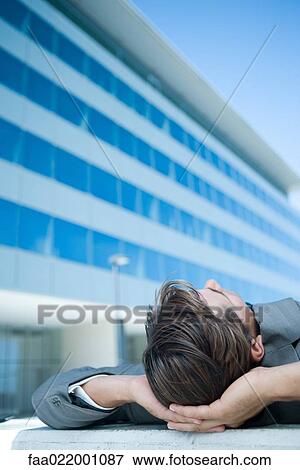 Businessman lying on ground outdoors, hands behind head, cropped view View Large Photo Image Stock Photo - Businessman lying on ground outdoors, hands behind head, cropped view. Fotosearch